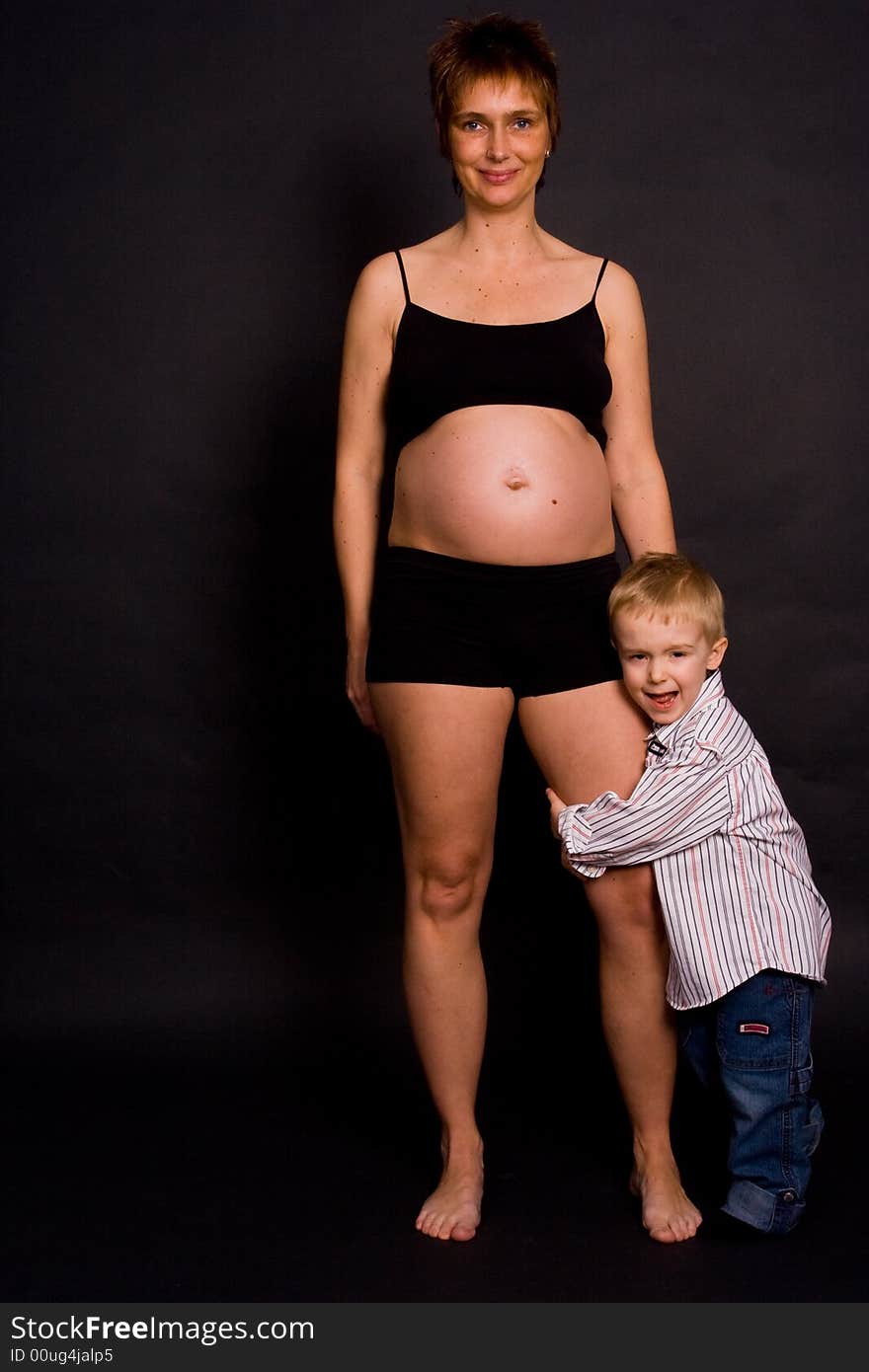 A pregnant woman with her child holding her leg. A pregnant woman with her child holding her leg