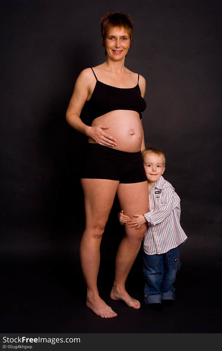 A pregnant woman with her child holding her leg. A pregnant woman with her child holding her leg