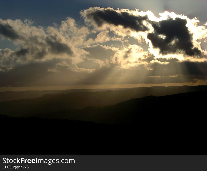 Sunbeams from behind clouds, with distant hills