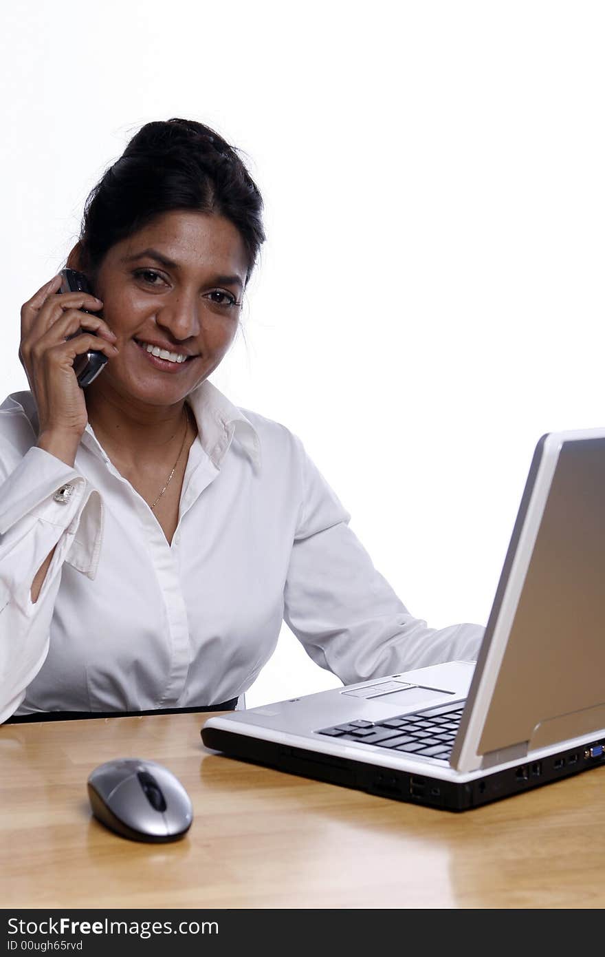 Indian business woman smiling on her cell phone while working at her laptop. Isolated against a white background. Indian business woman smiling on her cell phone while working at her laptop. Isolated against a white background