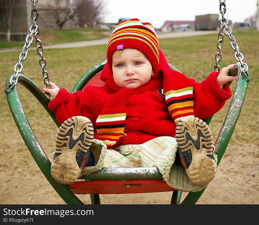 The sad girl in a red jacket goes for a drive on a swing