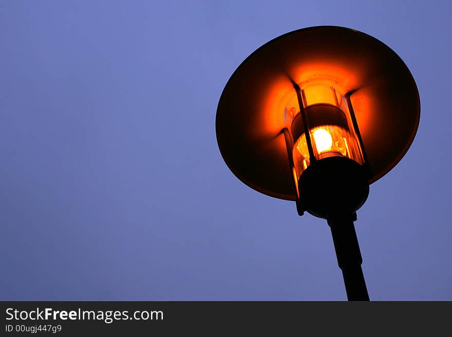 Street lamp isolated against pale blue sky with a soft orange glow.