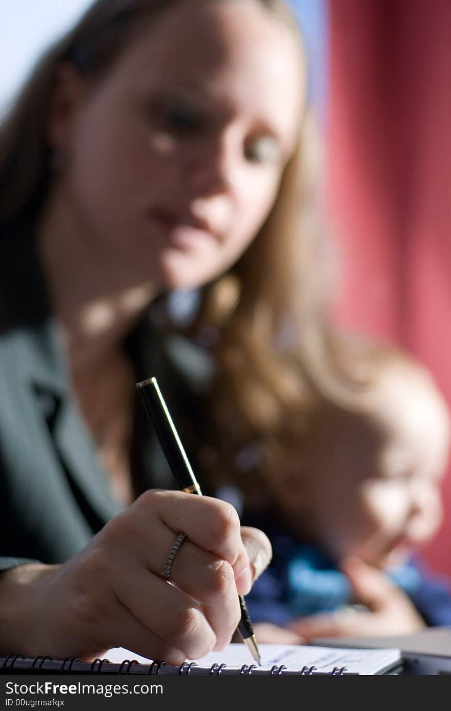 A woman writing a note while holding her baby boy. A woman writing a note while holding her baby boy.