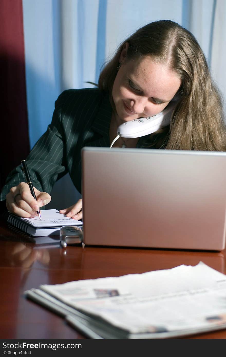 A woman sitting note taking and talking on cellphone. A woman sitting note taking and talking on cellphone.