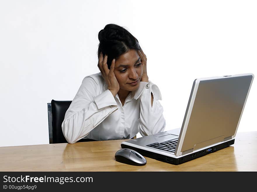 East Indian business woman sitting in front of her laptop holding her head in her hands. Isolated against a white background. East Indian business woman sitting in front of her laptop holding her head in her hands. Isolated against a white background