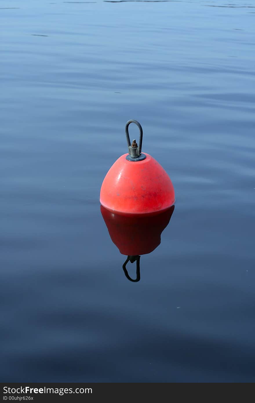 Red-orange plastic buoy with iron loop on the blue water. Red-orange plastic buoy with iron loop on the blue water