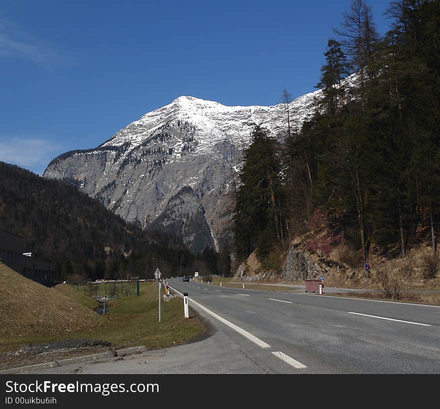 Road under the Peak of mountain at the background of blue sky . Alpes in Austria . The Snow on the Rocks. Road under the Peak of mountain at the background of blue sky . Alpes in Austria . The Snow on the Rocks.