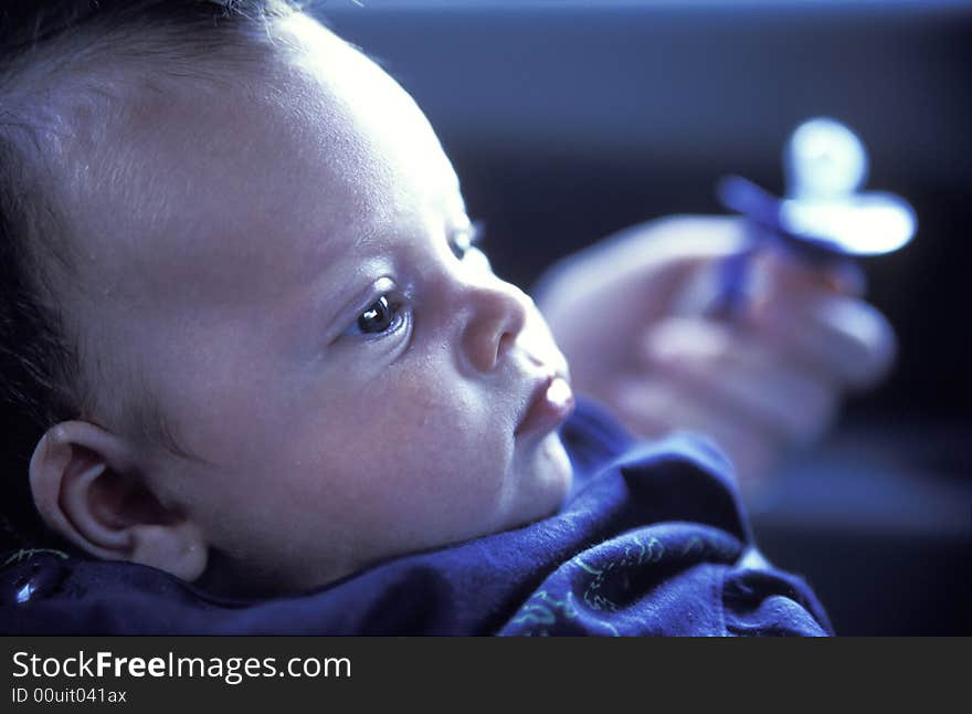 Boy baby profile portrait with unhappy expression. Adult hand in background holding pacifier.