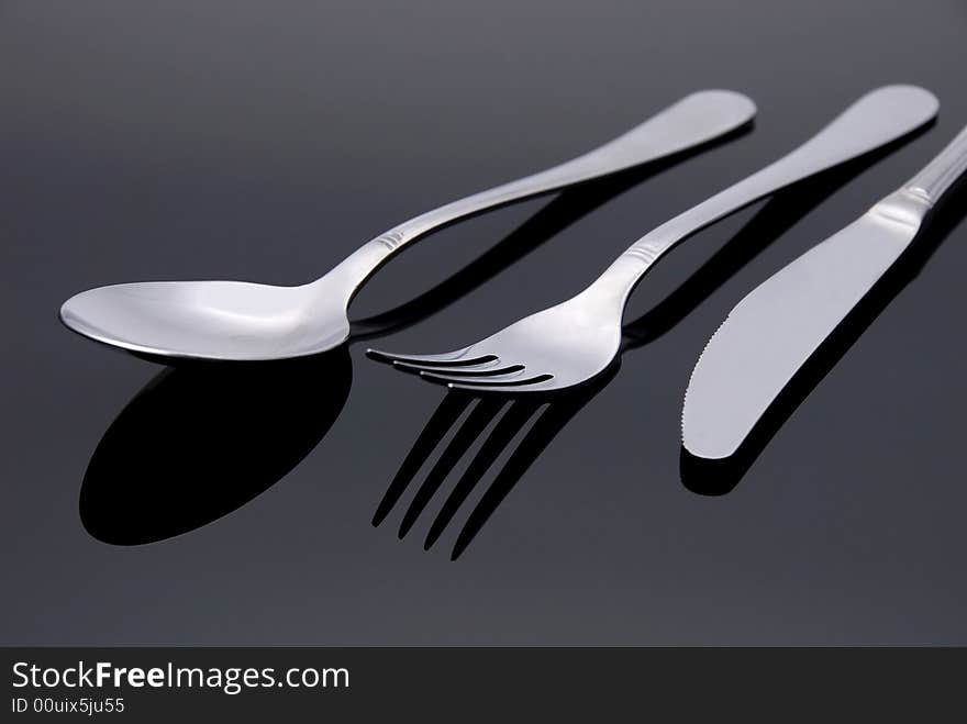 Modern silver spoon, knife, fork on the mirror background