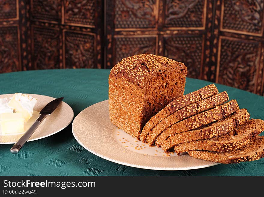 Freshly baked sliced wholegrain bread on a plate.  Sliced camerbert cheese and fresh butter in the background.