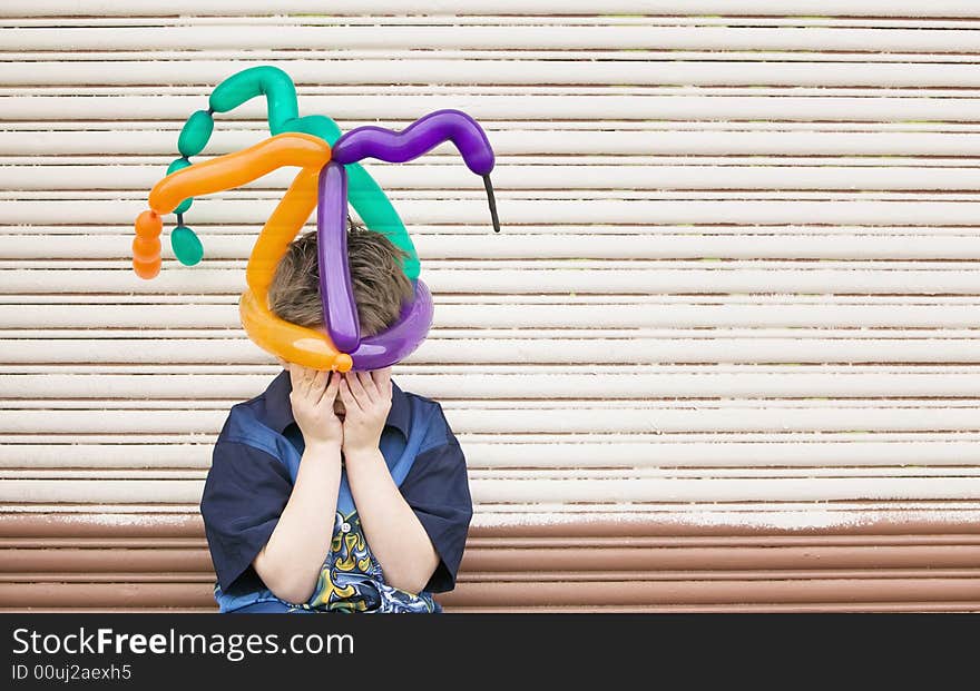 Young boy wearing a balloon hat hides his face. Young boy wearing a balloon hat hides his face