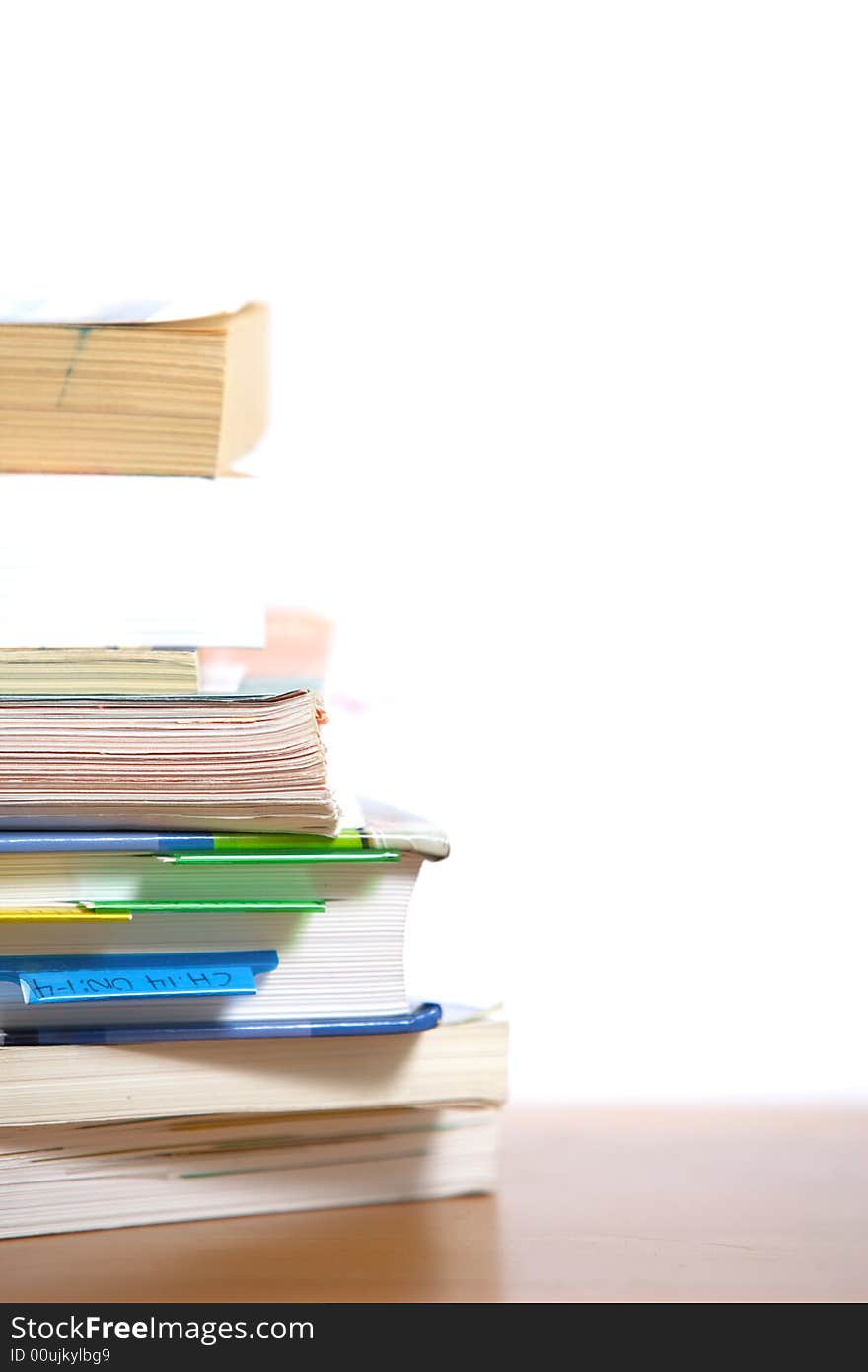 A stack of books sitting on the corner of a desk