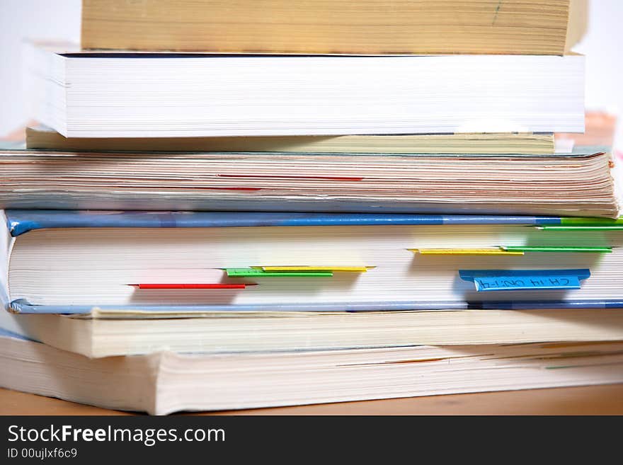 A stack of books sitting on the corner of a desk