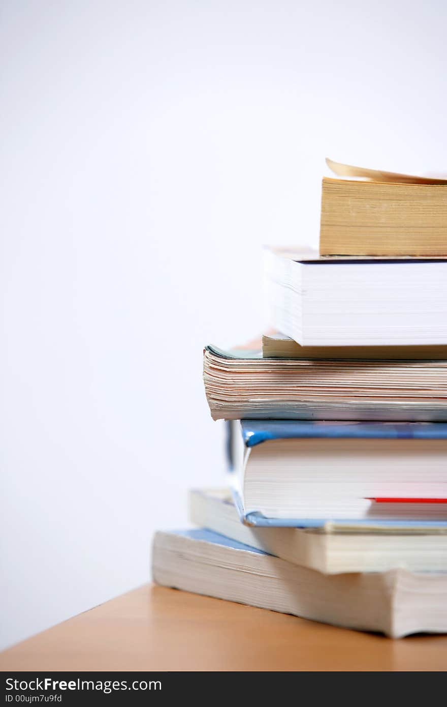 A stack of books sitting on the corner of a desk