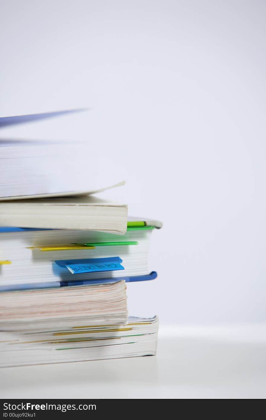 A stack of books sitting on the corner of a desk