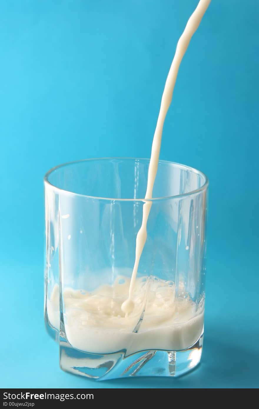 Milk poured in glass with blue background