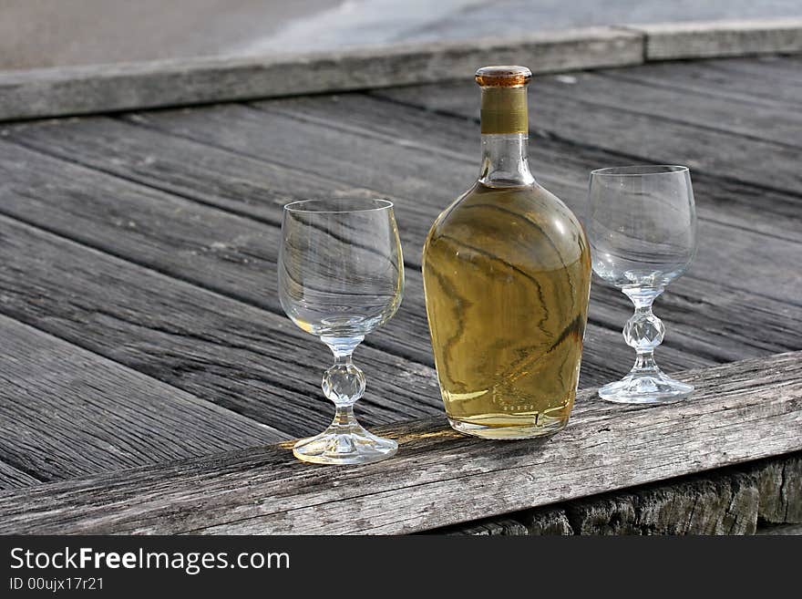 Beautiful vintage yellow bottle of wine and two crystal glasses on the boardwalk. Beautiful vintage yellow bottle of wine and two crystal glasses on the boardwalk