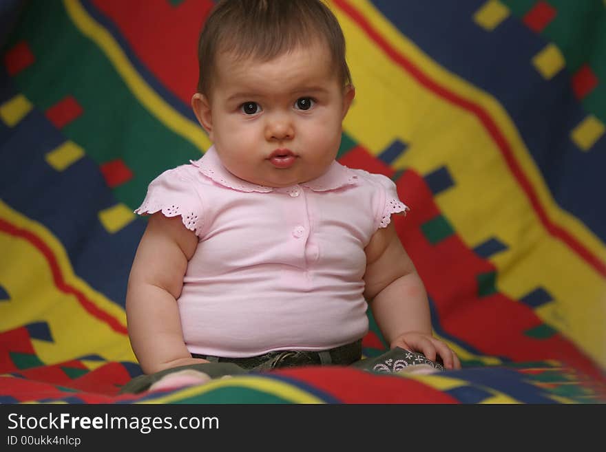 Small baby girl sitting on the colorful bedding. Small baby girl sitting on the colorful bedding