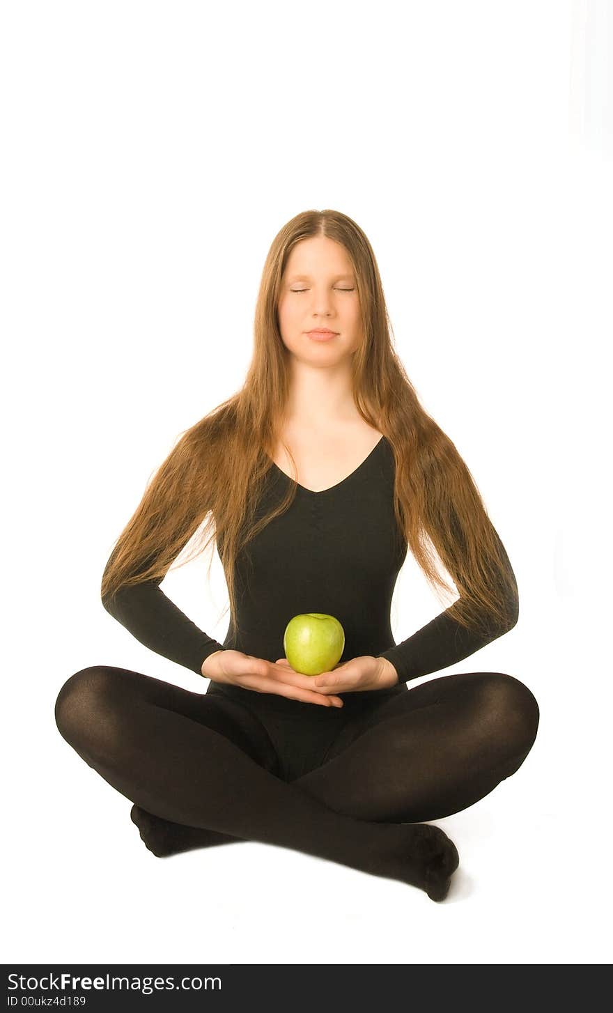 The portrait of a woman in lotus pose with a green apple in her hands. The portrait of a woman in lotus pose with a green apple in her hands