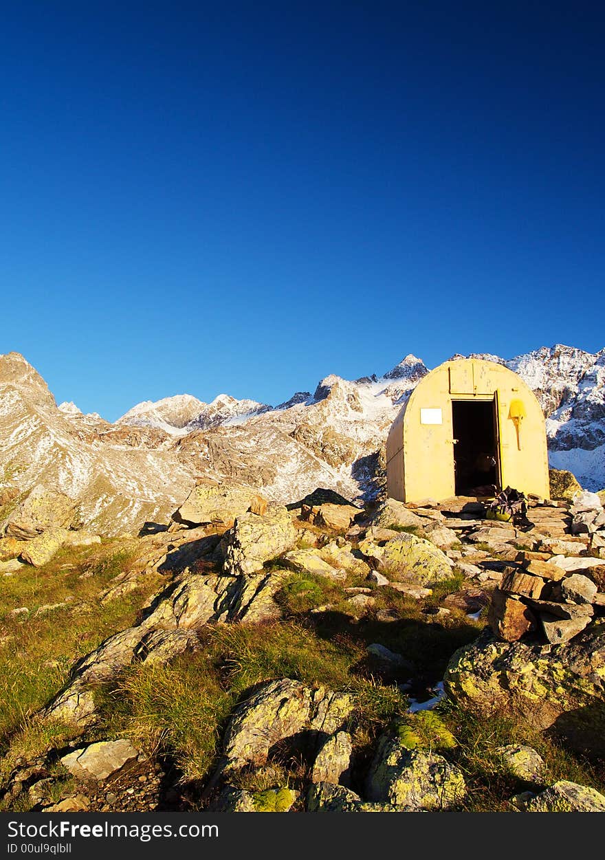 A yellow bivouac in a mountain landscape with a deep blue sky and snow