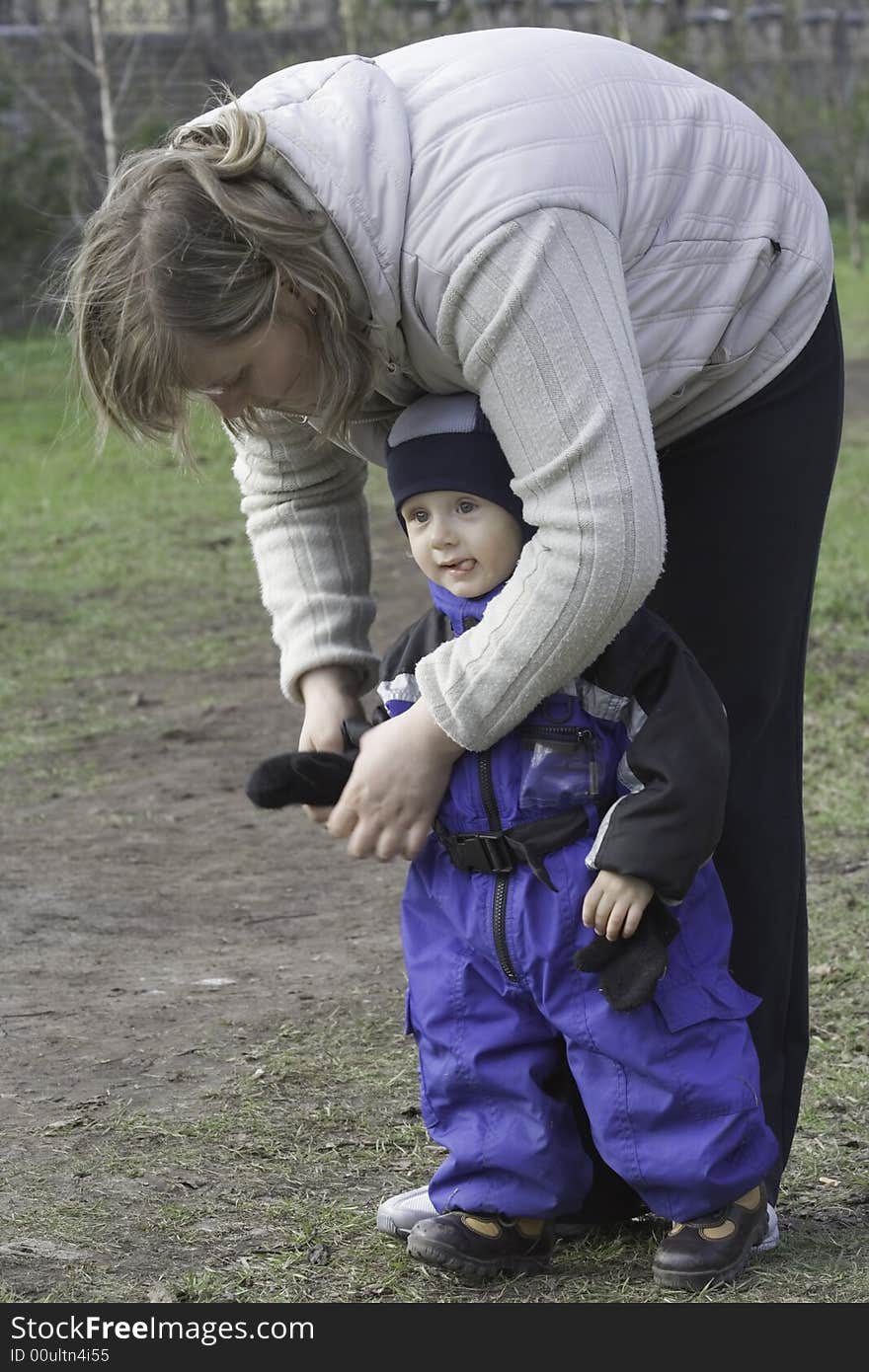 Mother dresses a glove to the small son in a blue overalls. Mother dresses a glove to the small son in a blue overalls