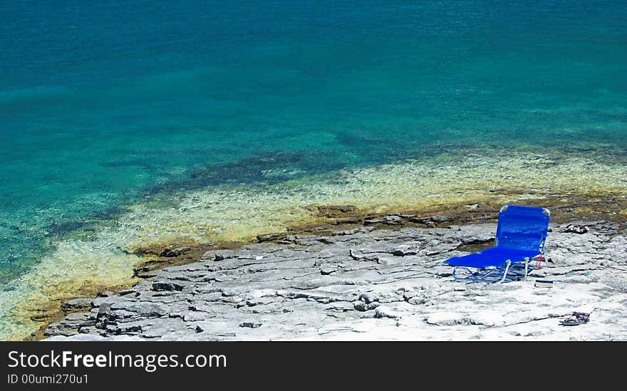 Lonely blue deckchair on a beautiful rocky beach. Lonely blue deckchair on a beautiful rocky beach