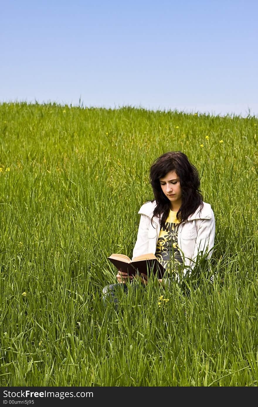 Young woman reading a book in a meadow