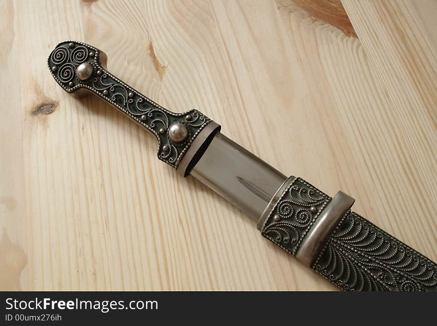 Traditional Georgian steel dagger in pattern stamping sheath on wooden background. Traditional Georgian steel dagger in pattern stamping sheath on wooden background