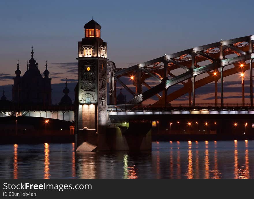 Illuminated bridge across Neva river against the background of the sunset