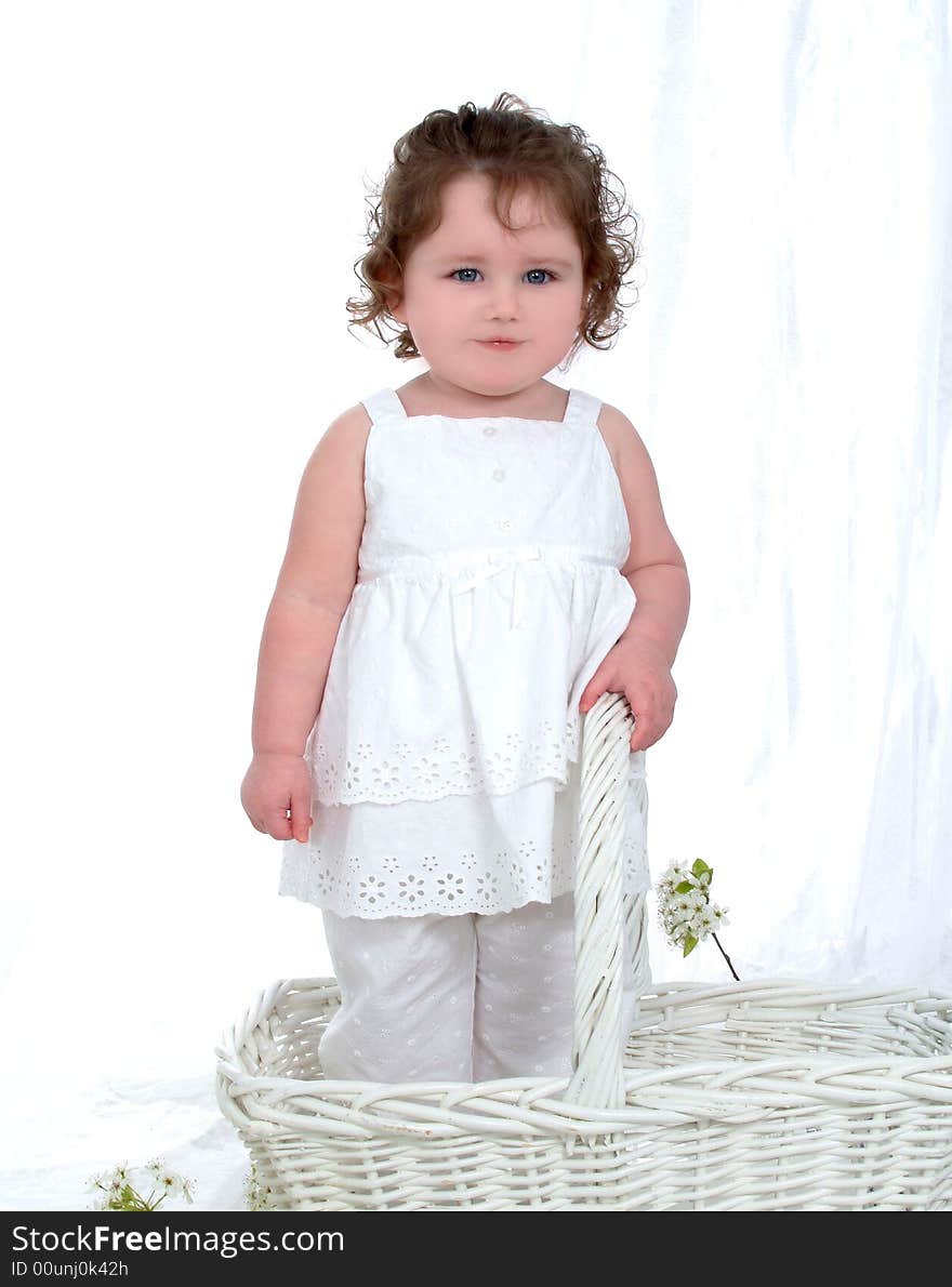 Baby girl in wicker basket in front of white background with flowers on floor and chick perched on flowers. Baby girl in wicker basket in front of white background with flowers on floor and chick perched on flowers