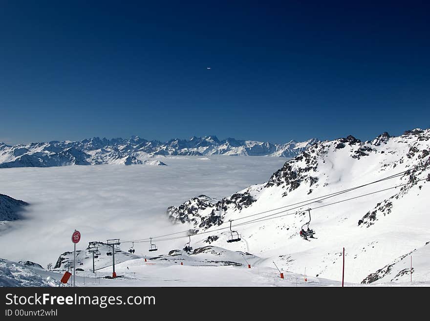 A ski lift and a ski slope sign, above the clouds