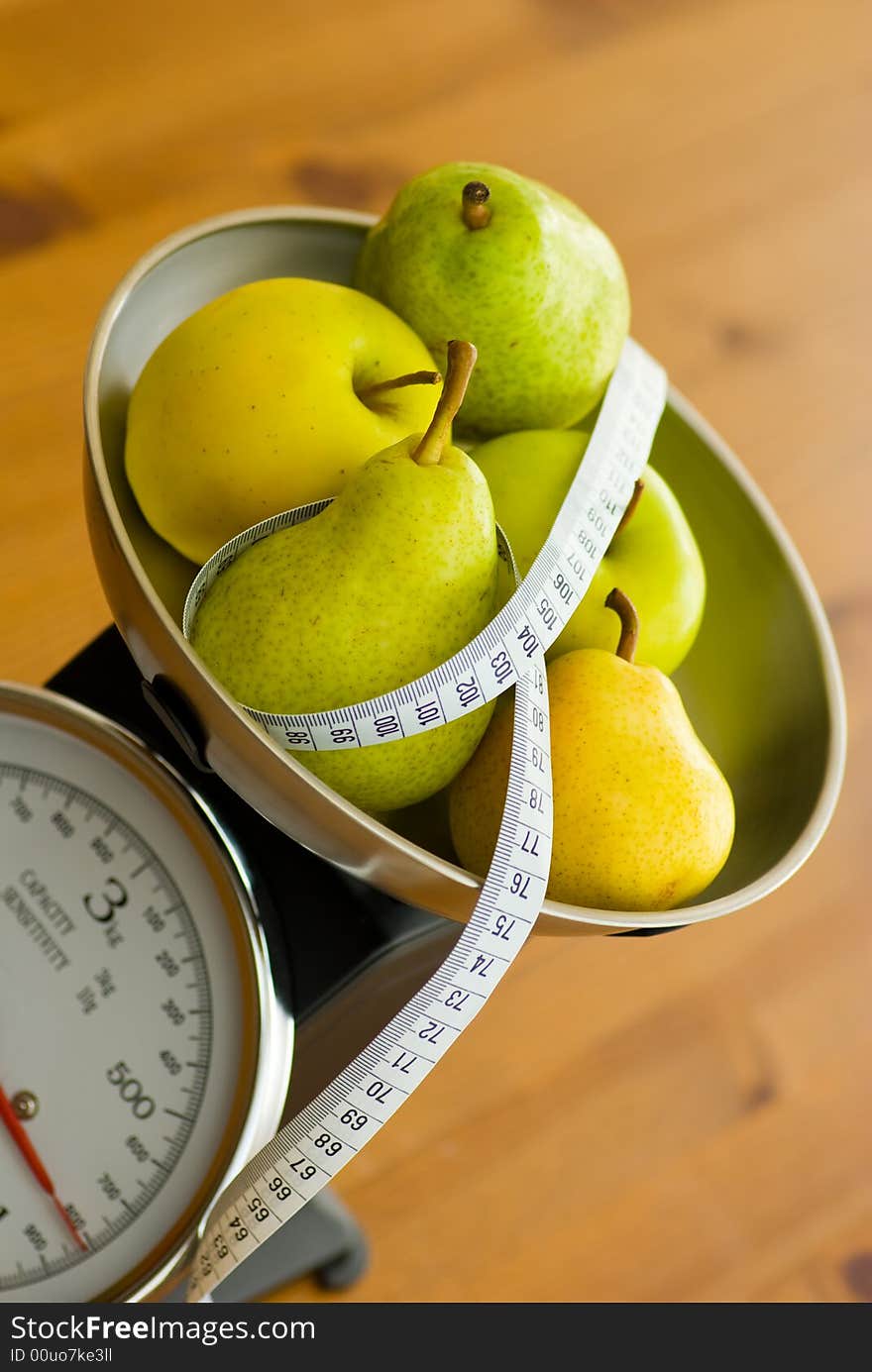 Apple and pear on kitchen scales with tape measure. Apple and pear on kitchen scales with tape measure