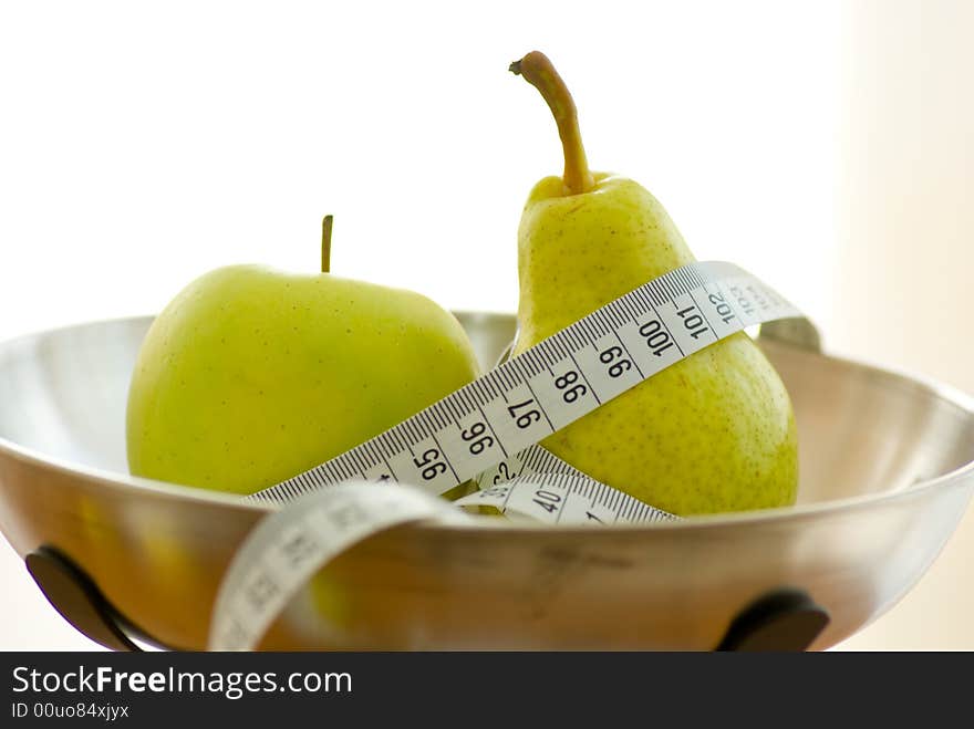 Apple and pear on kitchen scales with tape measure. Apple and pear on kitchen scales with tape measure