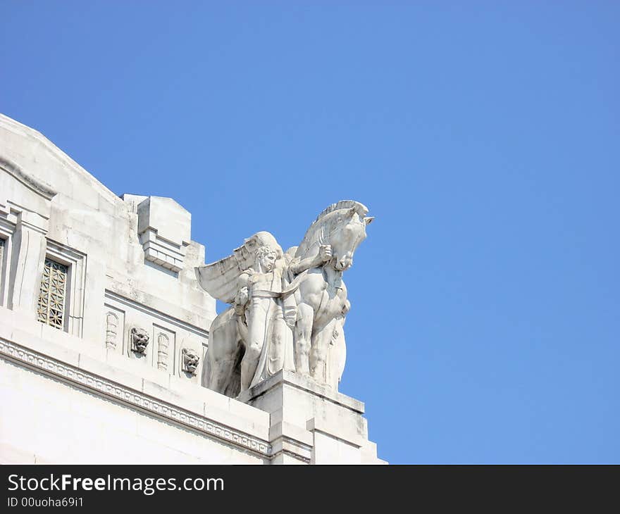 A statue of the train station of Milan, under a blue sky. A statue of the train station of Milan, under a blue sky