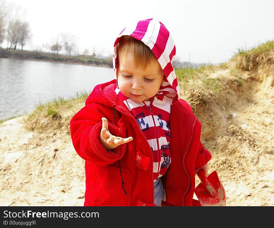 Little girl plays with sand on coast of lake. Little girl plays with sand on coast of lake