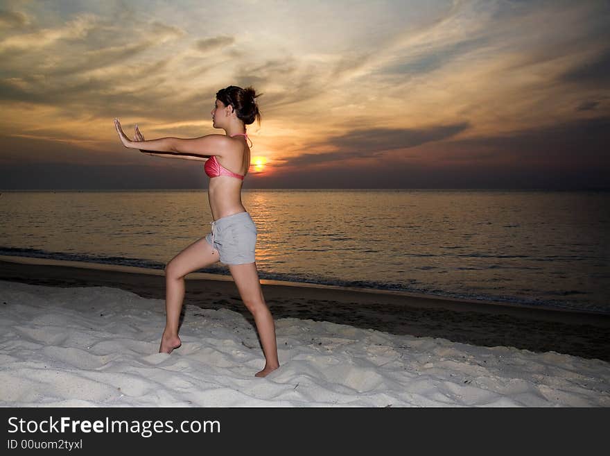 Woman doing yoga by the sunset beach