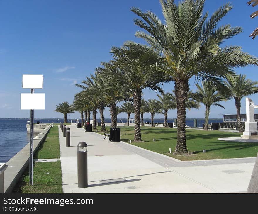 A park with straight rows of palm trees, benches, trash cans, a well manicured lawn and concrete slab overlooks the ocean. A park with straight rows of palm trees, benches, trash cans, a well manicured lawn and concrete slab overlooks the ocean.