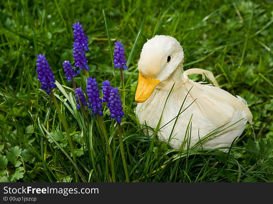 A handmade duck, made of straw and feathers,  beside purple flowers, amidst tall grass. A handmade duck, made of straw and feathers,  beside purple flowers, amidst tall grass.