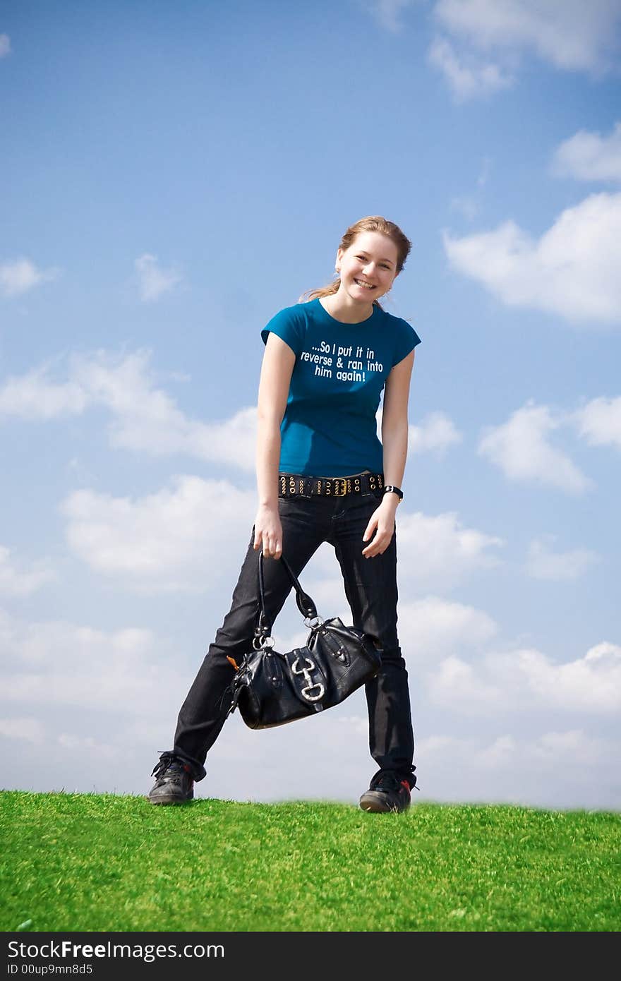 The young attractive girl with a handbag on a background of the blue sky