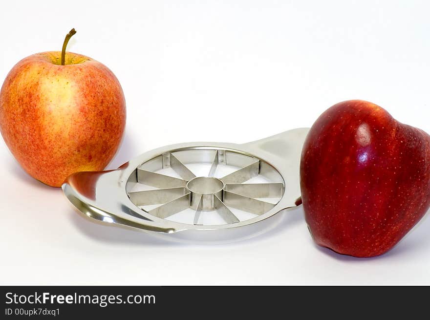 A view of two delicious red apples next to a handy, stainless steel apple slicer on a white background. A view of two delicious red apples next to a handy, stainless steel apple slicer on a white background.