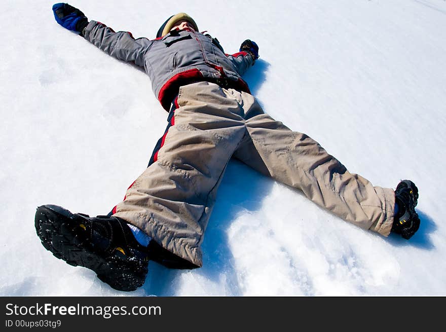 Tired boy lies in the snow and starts to make a snow angel. Tired boy lies in the snow and starts to make a snow angel