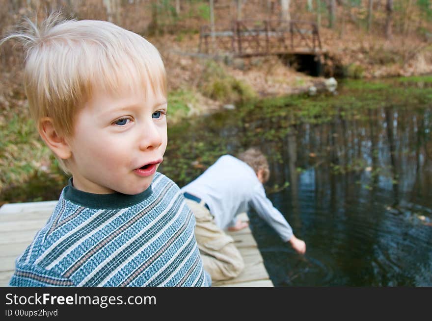 Two boys play on a dock by a scenic pond. Two boys play on a dock by a scenic pond