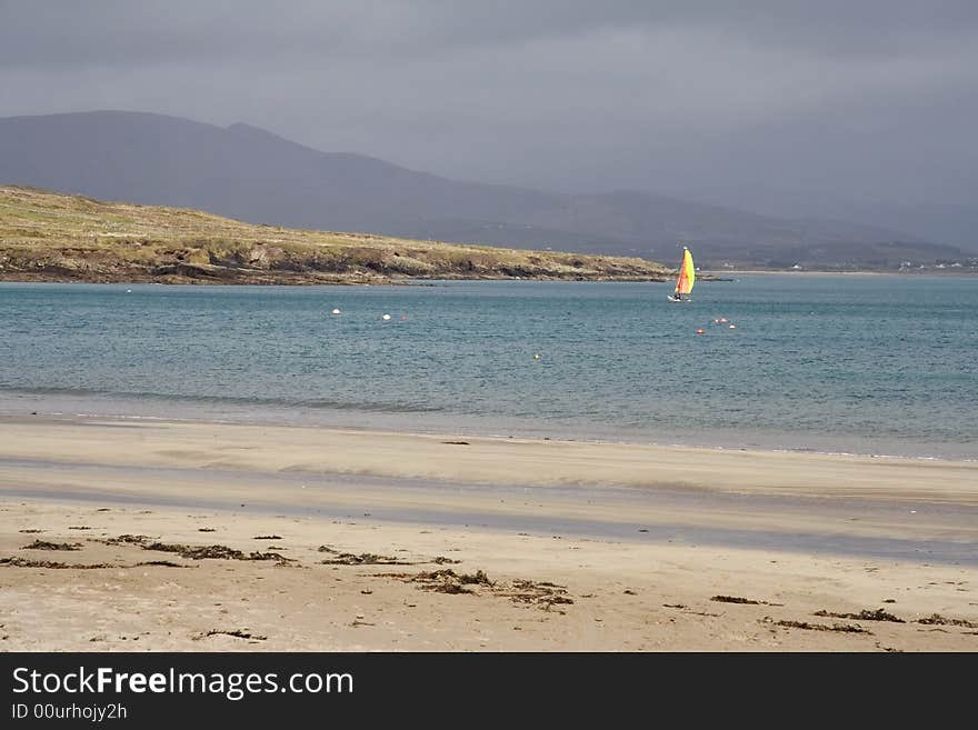 Windsurfer out at sea with sand dunes and a sandy beach in the foreground. Windsurfer out at sea with sand dunes and a sandy beach in the foreground