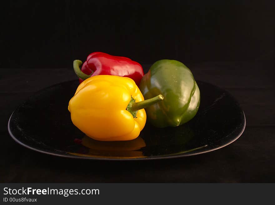 Three Peppers on Black in the Plate (Red, Green, Yellow). Three Peppers on Black in the Plate (Red, Green, Yellow)