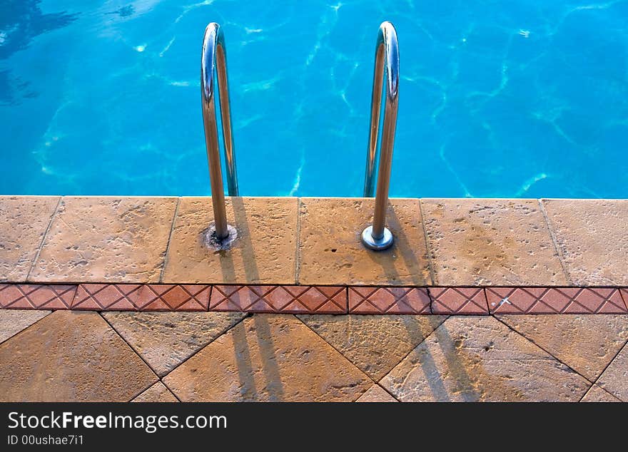 The concrete side of the swimming pool with the silver stairs. The concrete side of the swimming pool with the silver stairs