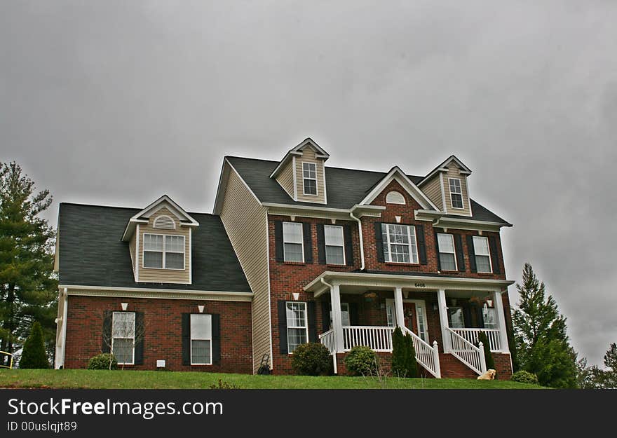 Large three story brick home with dormer windows and a landscaped yard.