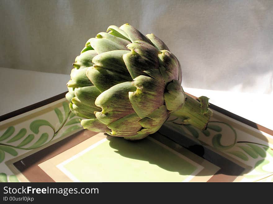 Still life of an artichoke sitting on a plate.