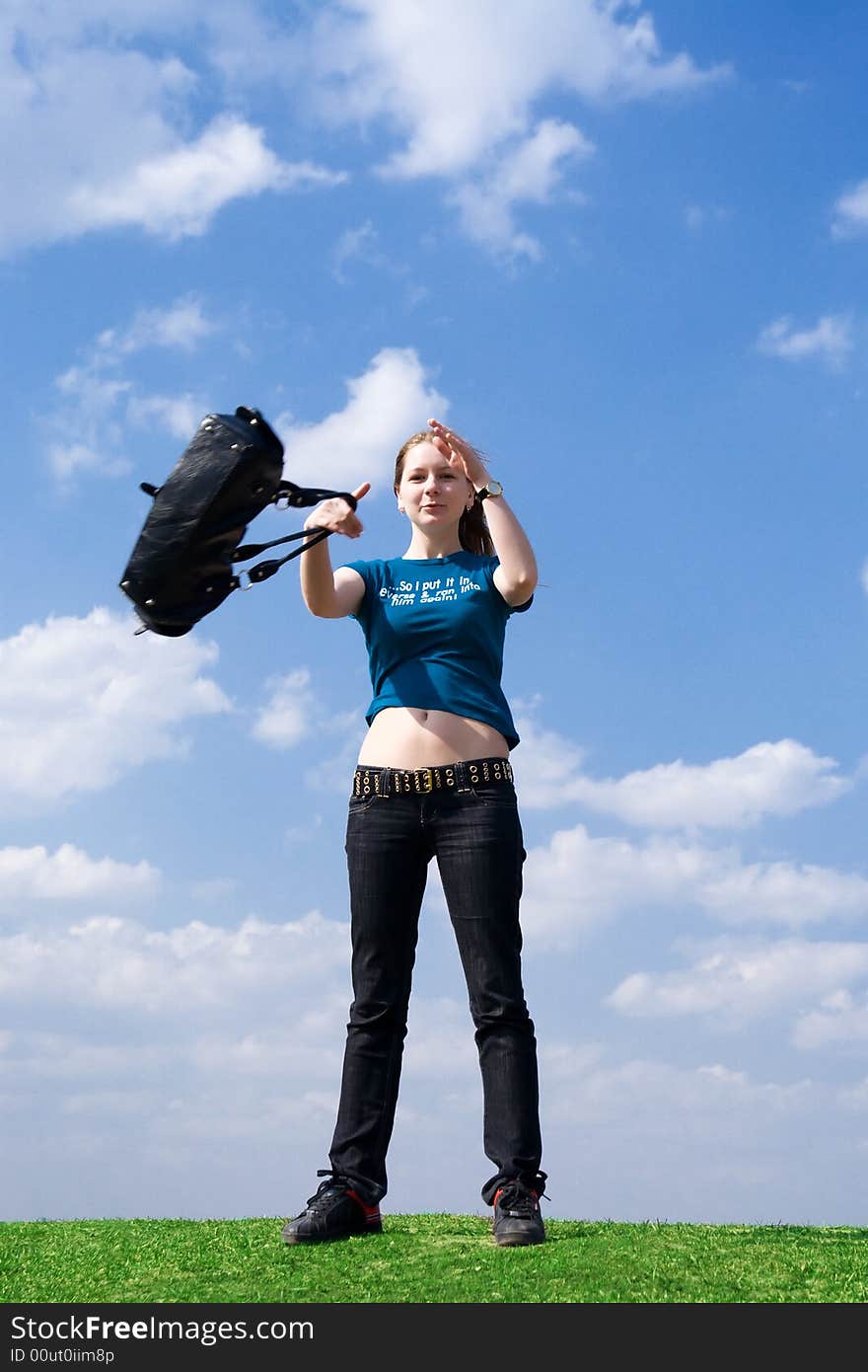 The young attractive girl with a handbag on a background of the blue sky