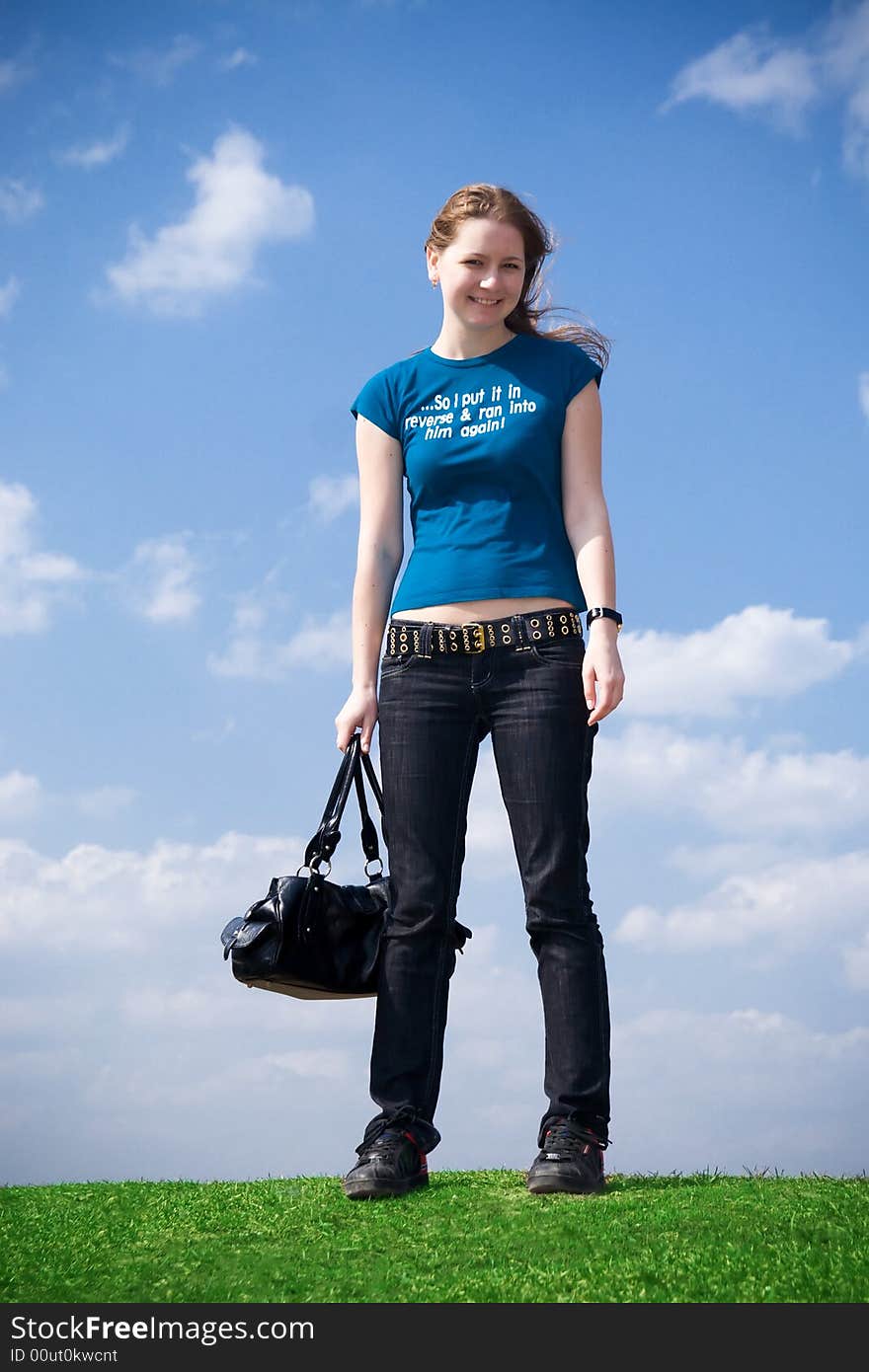 The young attractive girl with a handbag on a background of the blue sky