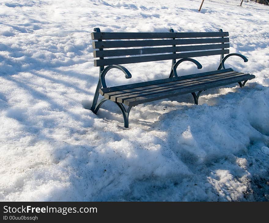 Park bench in the thawing snow at sunset